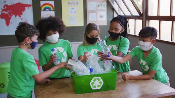 Group of kids wearing face masks putting plastic items in recycle container