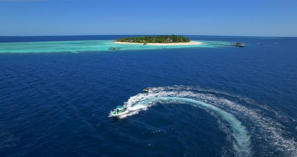 Aerial drone view of man and woman on an inflatable tube towing behind a boat to a tropical island.