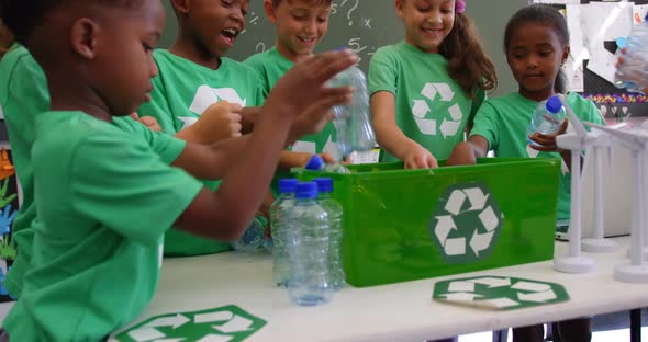 Mixed-race schoolkids putting recycle bottles in the tray at classroom 4k