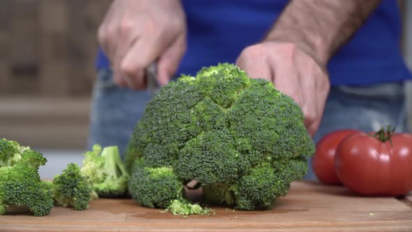 A Man in the Kitchen Cuts Fresh Green Broccoli with a Knife Closeup