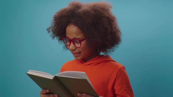 African American school girl in eye glasses reads book and smiles at camera