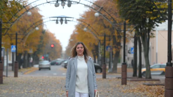 young happy blonde girl in coat walks along the street of the autumn city