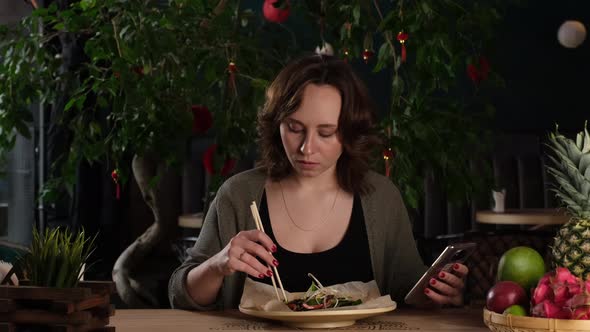 Beautiful Girl Eats Salad and Looks at the Phone