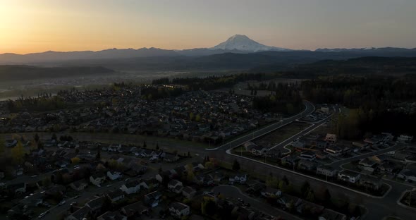 Wide aerial of Mount Rainier at sunrise with neighborhoods in the foreground.