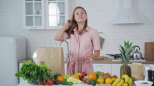 Lovely young woman takes out of a bag organic fruit in the light kitchen.