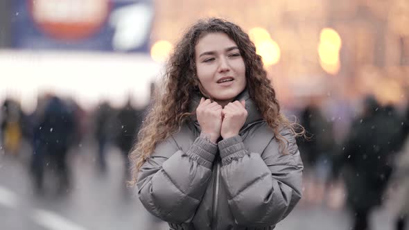 Portrait of a Young Woman with Curly Hair Standing on a Crowded City Street on a Cold Day