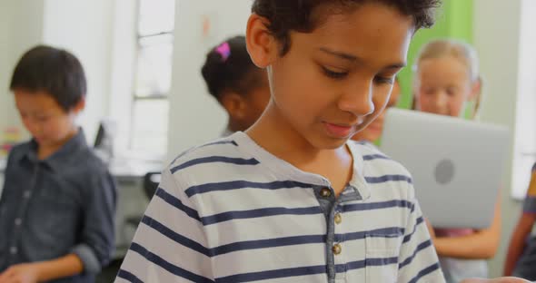 Cute mixed-race schoolboy using digital tablet in classroom at school 4k