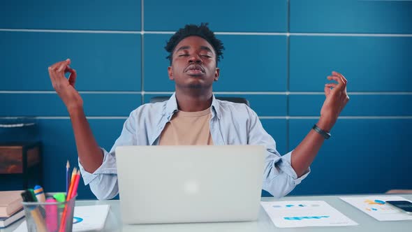 Young African American Man Student Meditates Sits at Table with Laptop