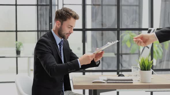 Colleague passes a paper tablet with documents. Businessman feels overjoyed. Happy man reads good ne