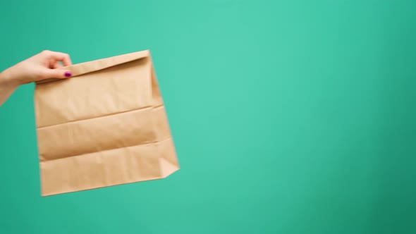 Courier in Gloves Passing Craft Shopping Bag with Delivery Against Mint Background