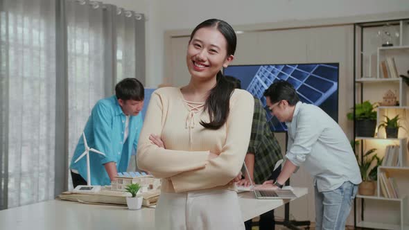 Smiling Asian Woman Engineer Crossing Her Arms To Camera While Her Colleagues Are Discussing Work