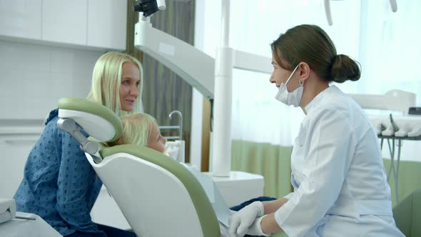 Little Girl Sits in a Dental Chair, Her Mother Talks To a Doctor 