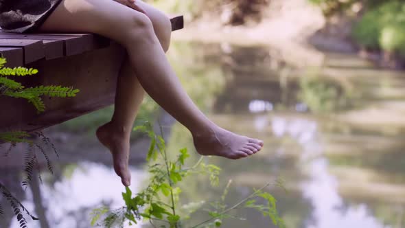 slow-motion of woman's legs hanging over edge of a wooden jetty