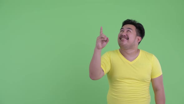 Happy Young Overweight Asian Man Pointing Up and Looking Surprised