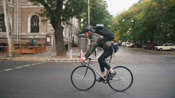 Young Hipster Man in Helmet Riding Fixed Gear Bicycle in the City During Autumn Morning Side View