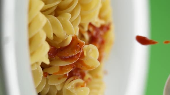 Vertical video: tomato paste falls on pasta in a plate