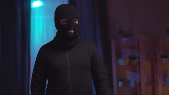Thief in a Black Balaclava with a Flashlight in the House