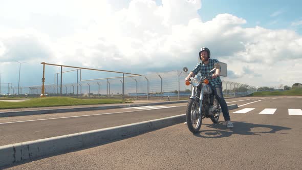 Young Man Biker with Custom Motorcycle on Street at Sunset