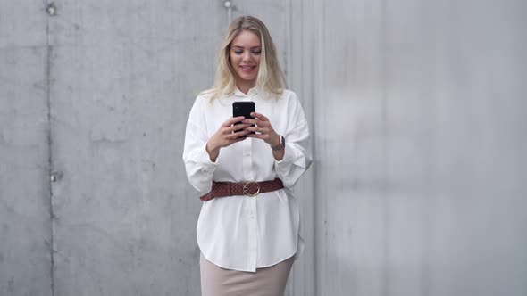 Young Woman Using Smartphone Near Wall