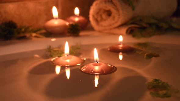 relaxing spa background with candles floating in the bath water, some green petals and a towel near