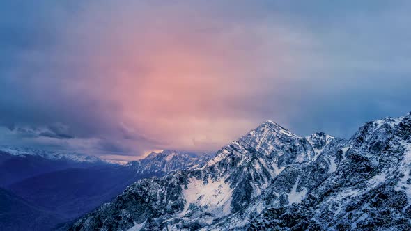 Snowcapped mountains zooming in to time lapse animated cloudscape during a dark sunrise or sunset