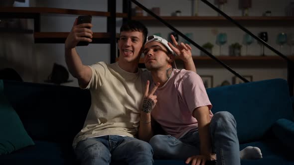 Cheerful Loving Happy Gay Couple Making Faces Gesturing Peace Taking Selfie on Smartphone