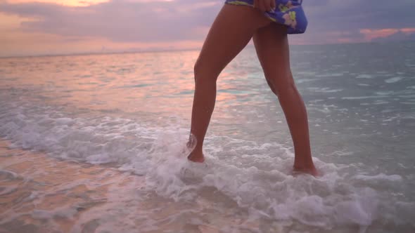 Female Legs Walking on the Beach Edge Enjoying Fresh Ocean Waves Charming Pink Sunset Reflection