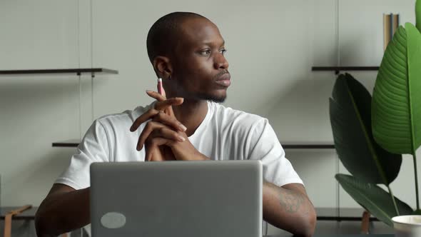 Thoughtful Black Businessman Sitting at a Desk with a Computer and Looking Away