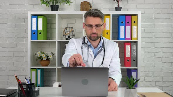 Remote doctor wears white medical coat in hospital office opens using laptop
