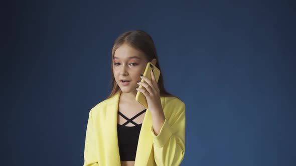 A Young Teenage Girl Talking on the Phone Against a Blue Background