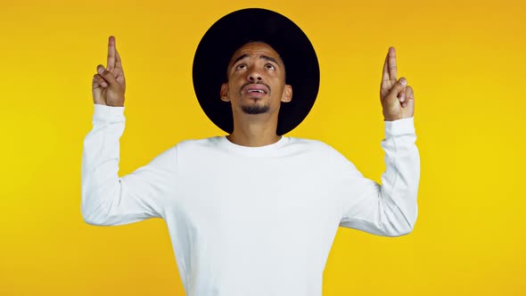 Young Hipster African Man in Black Hat Praying Over Yellow Background. Guy Begging Someone Satisfy