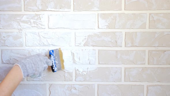 The master's hand paints a wall of decorative bricks with a brush with white paint with his own hand