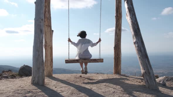 Back view of woman on wooden swing enjoying view from top of Folgosinho mount. Freedom concept