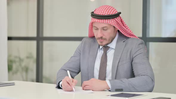 Middle Aged Arab Businessman Writing on Paper in Office