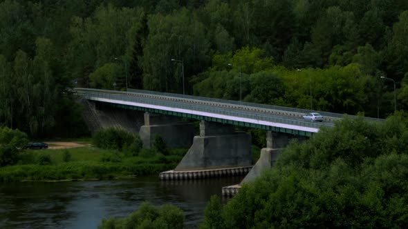 Moody shot of car driving on a bridge with green forest around it.