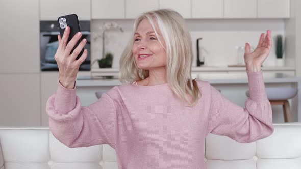 Cheerful Gray Hair Woman Talking To Smartphone Video Call Conference at Home Sitting on Sofa