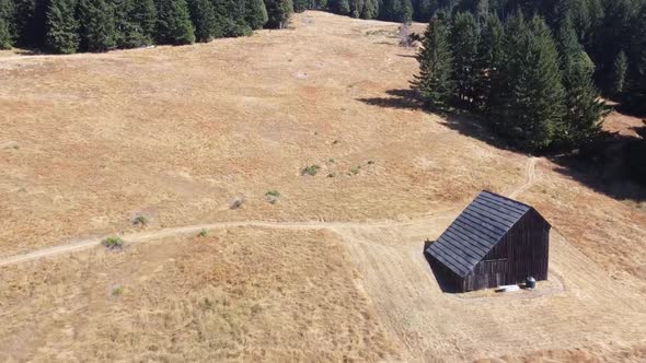 Drone Flying Over A Field In a Forested Area With A Barn