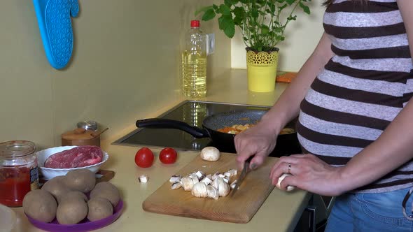 Pregnant Woman Hands Cutting Champion Mushrooms with Knife on Board in Kitchen