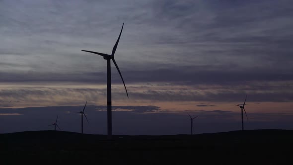 Motion the Blades of a Large Wind Turbine in a Field Against a Background of Sunset on the Horizon