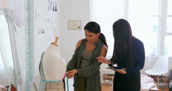 Fashion designers using tablet while measuring dress makers model 