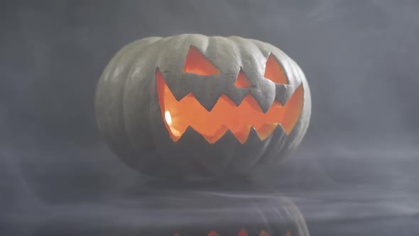 Smoke effect over scary face carved halloween pumpkin against grey background