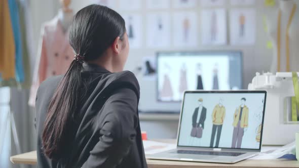 Back View Of Asian Female Designer In Business Suit Having A Backache While Designing Clothes