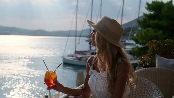 Woman in Straw Hat Drinking Aperol Spritz Cocktail Sitting at Summer Cafe Terrace at Ermioni Greece