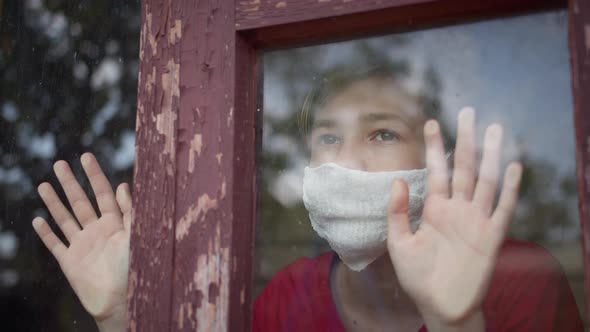 Boy in Mask Sits at Home Looks Outside and Takes Off the Mask