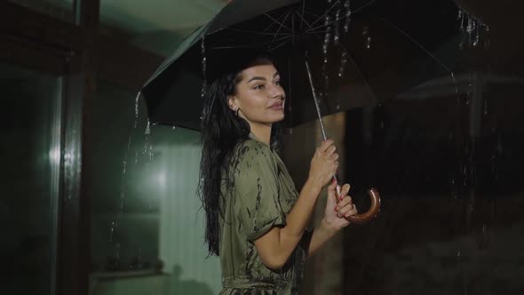 Happy Girl with Umbrella in Hand Poses Under the Night Rain at Home