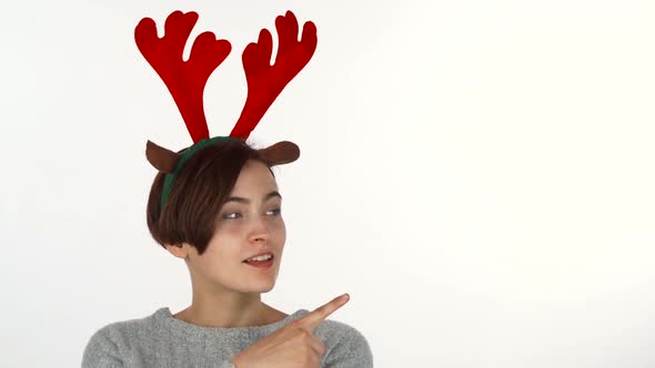 Young Woman Wearing Reindeer Antlers Headband Pointing at the Copy Space