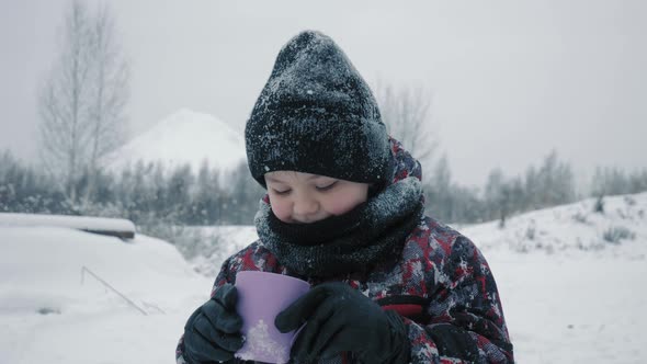 Cheerful boy drinking hot tea from cup in snowy forest at winter walk