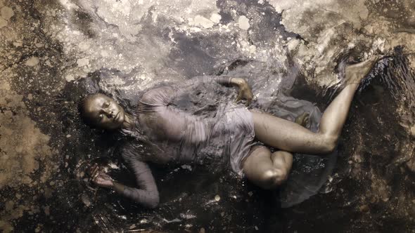 A Woman in a Dress with Dyed Golden Skin and Hair Lies in the Water Slowly Moving and Posing