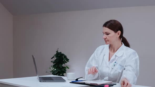 Female Doctor Looking Up Information on the Laptop in White Office