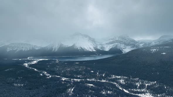 Drone camera shoots the Bow River flowing through a dark forest and Hector Lake in Alberta, Canada